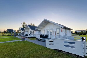 Una hilera de modernas casas móviles blancas con techos planos y ventanas amplias, dispuestas en fila sobre un césped bajo un cielo despejado.
