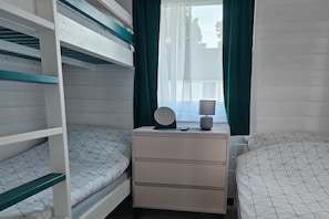 Une chambre avec un lit superposé, une table de chevet, une lampe et une fenêtre avec des rideaux.