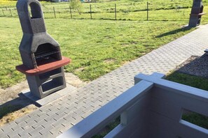 Un barbecue en pierre avec un panneau frontal rouge, installé sur un chemin pavé, avec une clôture métallique en arrière-plan.