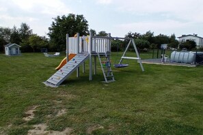 A playground with a slide, climbing wall, and swing set in a grassy area. - Family Holiday Homes, Playground, Summer Pool (Ustronie Morskie)