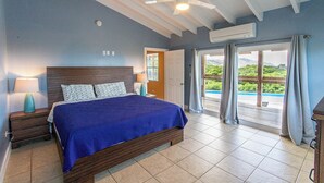Ein Schlafzimmer mit einem großen Bett, einem Deckenventilator und Blick ins Freie durch eine Schiebetür.
