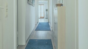 Un couloir étroit, avec un tapis bleu, des murs blancs et une porte au fond.