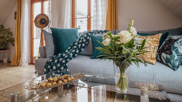 Un salon chaleureux avec un canapé, une table basse en verre sur laquelle sont posés des biscuits, un vase de fleurs et une lampe.