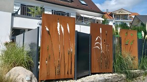 Une maison moderne avec un toit en pente, un balcon et une clôture en métal aux lignes verticales.