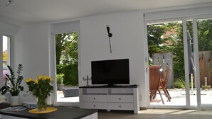 A modern living room with a flat-screen TV, a dining area, and a sliding glass door leading to an outdoor patio.