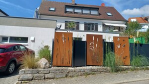 A modern two-story house with a flat roof, large windows, and a gated entrance.