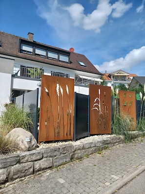 Une maison moderne avec un toit en pente, un balcon et une clôture en métal aux lignes verticales.