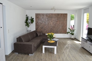 Un salon moderne avec un canapé d’angle, une table basse ornée d’un vase de fleurs et un grand tableau abstrait accroché au mur.