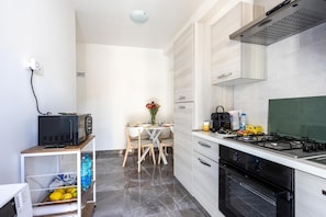 A modern kitchen with a gas stove, oven, and microwave. There is a dining table with chairs and a vase of flowers. - Rosina's House by Rentbeat (Roma)