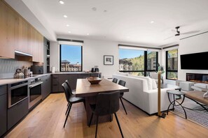 A modern kitchen with built-in appliances, a dining area with a wooden table and chairs, and a living area with a sofa and a fireplace. - Electric Pass Lodge 308 (Snowmass Village)