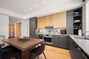 A modern kitchen with grey cabinetry, a wooden dining table, and a built-in oven. - Electric Pass Lodge 308 (Snowmass Village)