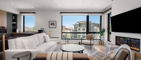 A modern living room with a white sofa, a round coffee table, a beige armchair, and a fireplace.