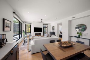 A modern living space with a large sofa, a dining table, and a flat-screen TV mounted on the wall.