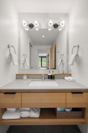 A modern bathroom with a large mirror, two sinks, and a vanity with storage drawers.