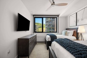A hotel room with a bed, bedside table, TV, and a window with a view of a building under construction. - Electric Pass Lodge 308 (Snowmass Village)