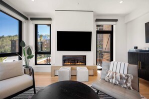 A modern living room with a fireplace, large windows, and a flat-screen TV.