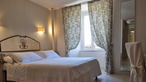 Una cama bien hecha en una habitación de hotel, con cabecera, lámpara de noche y una silla con funda.