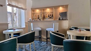 Zona de bar con suelo de mármol, sillas blancas y verdes, y una estantería con botellas.