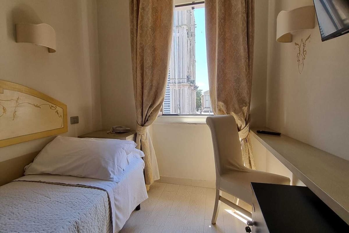 A hotel room with two beds, a desk, a chair, a TV, and a window with curtains.