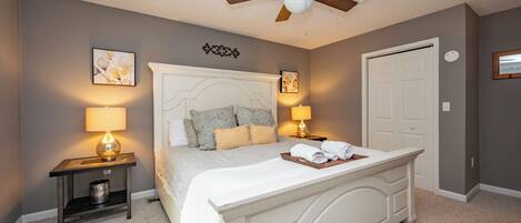 A bedroom with a bed, two bedside tables with lamps, a ceiling fan, and a door.