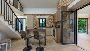 Een moderne keuken met een stenen muur, een houten trap en een glazen deur naar buiten.