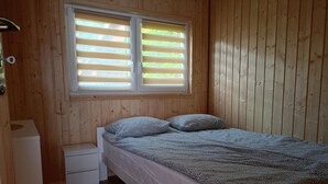 A wooden-paneled room with a bed, a small bedside table, and a window with blinds. - 2 Bedroom Holiday Home With air Conditioning (Postomino)