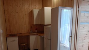 A compact kitchen with wooden walls, a white refrigerator, a sink, and a stool. - 2 Bedroom Holiday Home With air Conditioning (Postomino)