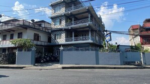 A multi-story residential building with balconies, a gated entrance, and a clear sky. - Hotel Mountain Village (Pokhara)