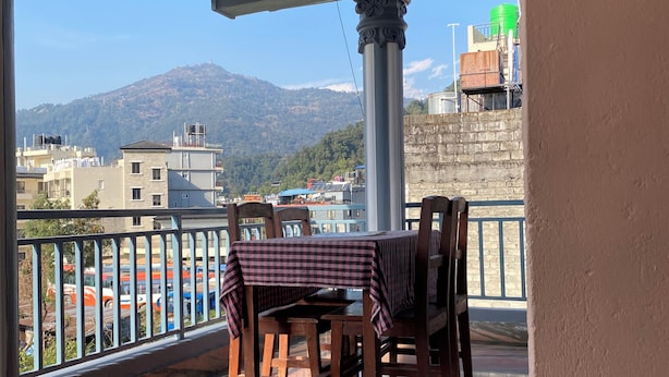 A balcony with a table and chairs, a view of a mountain, and a cityscape in the background. - Hotel Mountain Village (Pokhara)