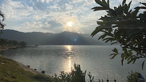 A serene lakeside view with a clear sky, calm water, and distant mountains. - Hotel Mountain Village (Pokhara)