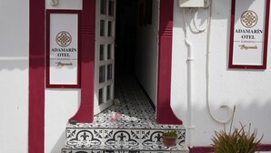 Entrada de un edificio con suelo de baldosas y una puerta que da al interior. Hay dos letreros en las paredes, uno a cada lado de la puerta, con el texto 