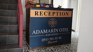 Una mesa de recepción con el rótulo "RECEPTION", el nombre "ADAMARIN OTEL" y un número de teléfono.