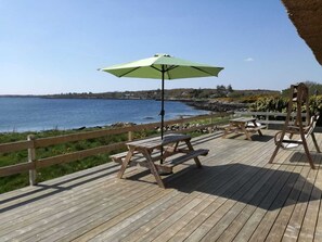 Een houten terras met picknicktafels en een parasol met uitzicht op het water.