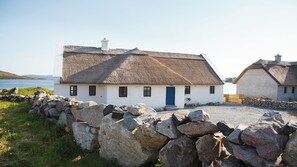 A white cottage with a thatched roof, a blue door, and a stone wall in front.