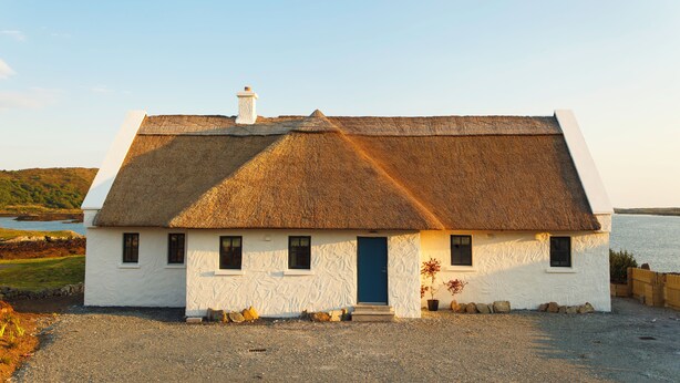 Una casa tradizionale con pareti bianche, tetto di paglia, una porta blu e vialetto in ghiaia.