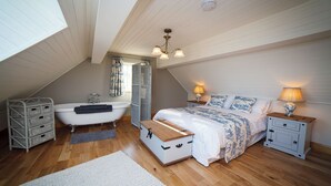 Una camera da letto con soffitto spiovente, una vasca, un letto con comodini coordinati e un settimino.
