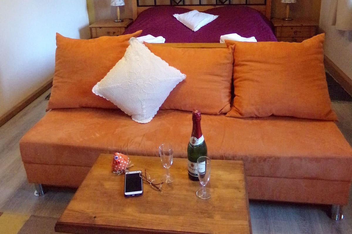 Une chambre d’hôtel avec un lit, des oreillers orange et blancs, une table en bois sur laquelle se trouve une bouteille de champagne, deux verres et un téléphone intelligent.
