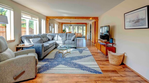 Un salon spacieux avec un grand canapé d’angle gris, une table basse en verre et un tapis à motifs bleus.