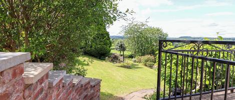 A brick wall with steps leading to a garden with a metal fence and a view of a green landscape.