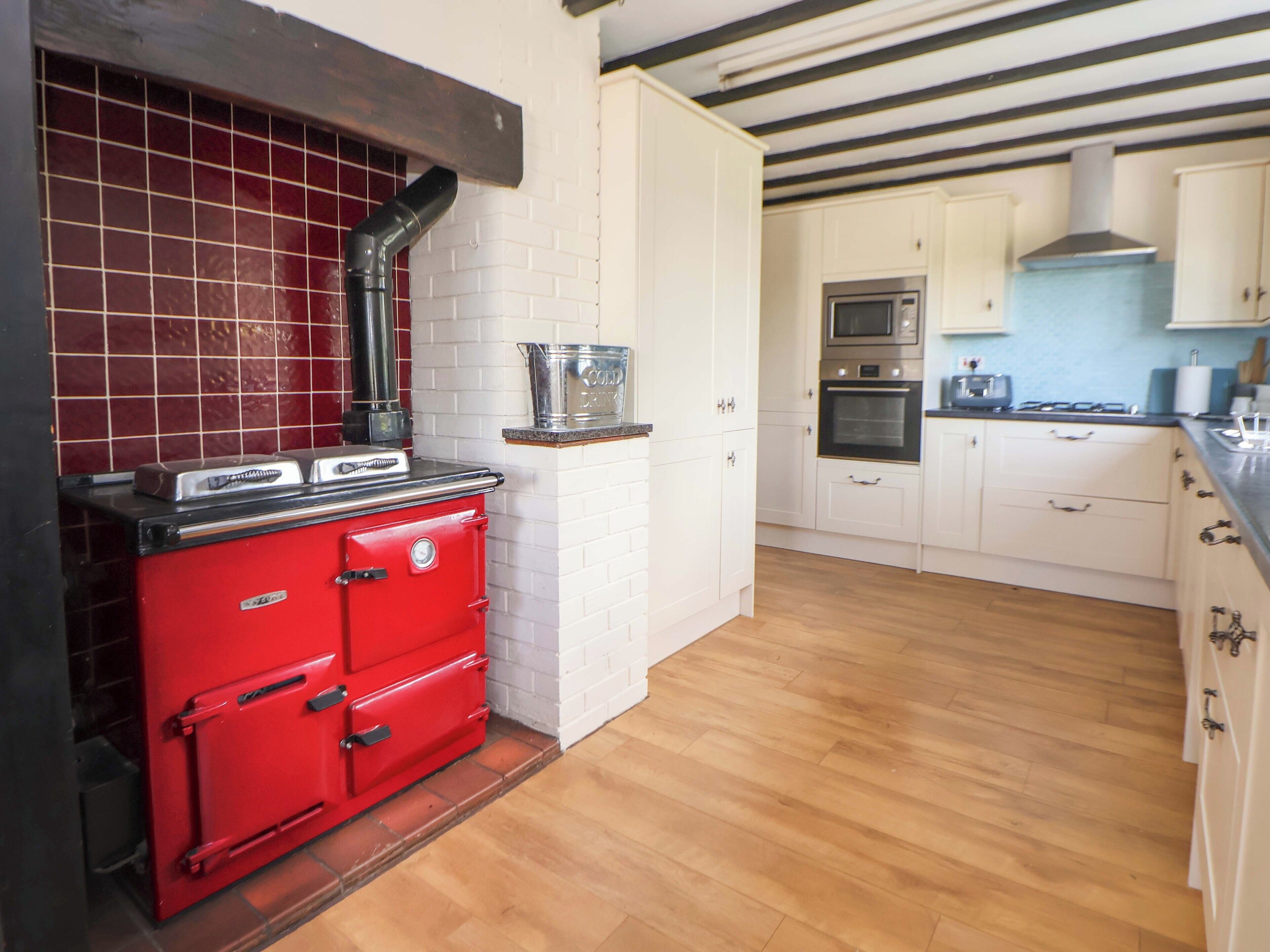 Una cocina con estufa roja, armarios blancos, salpicadero de azulejos y piso de madera.