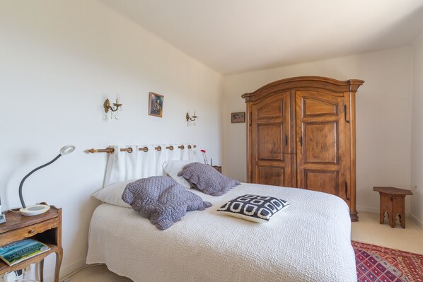 Une chambre à coucher avec un lit, une armoire en bois, une table de chevet avec une lampe et un petit tabouret.