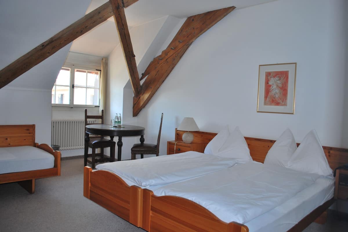 A bedroom with a wooden bed, a small round table, a chair, and a window with curtains.