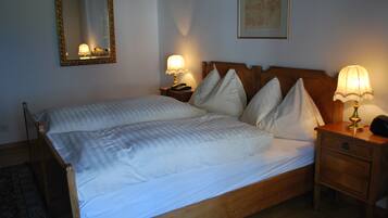 A neatly made bed with white linens and pillows, a wooden headboard, two bedside lamps, a nightstand with a telephone, and a framed picture on the wall.