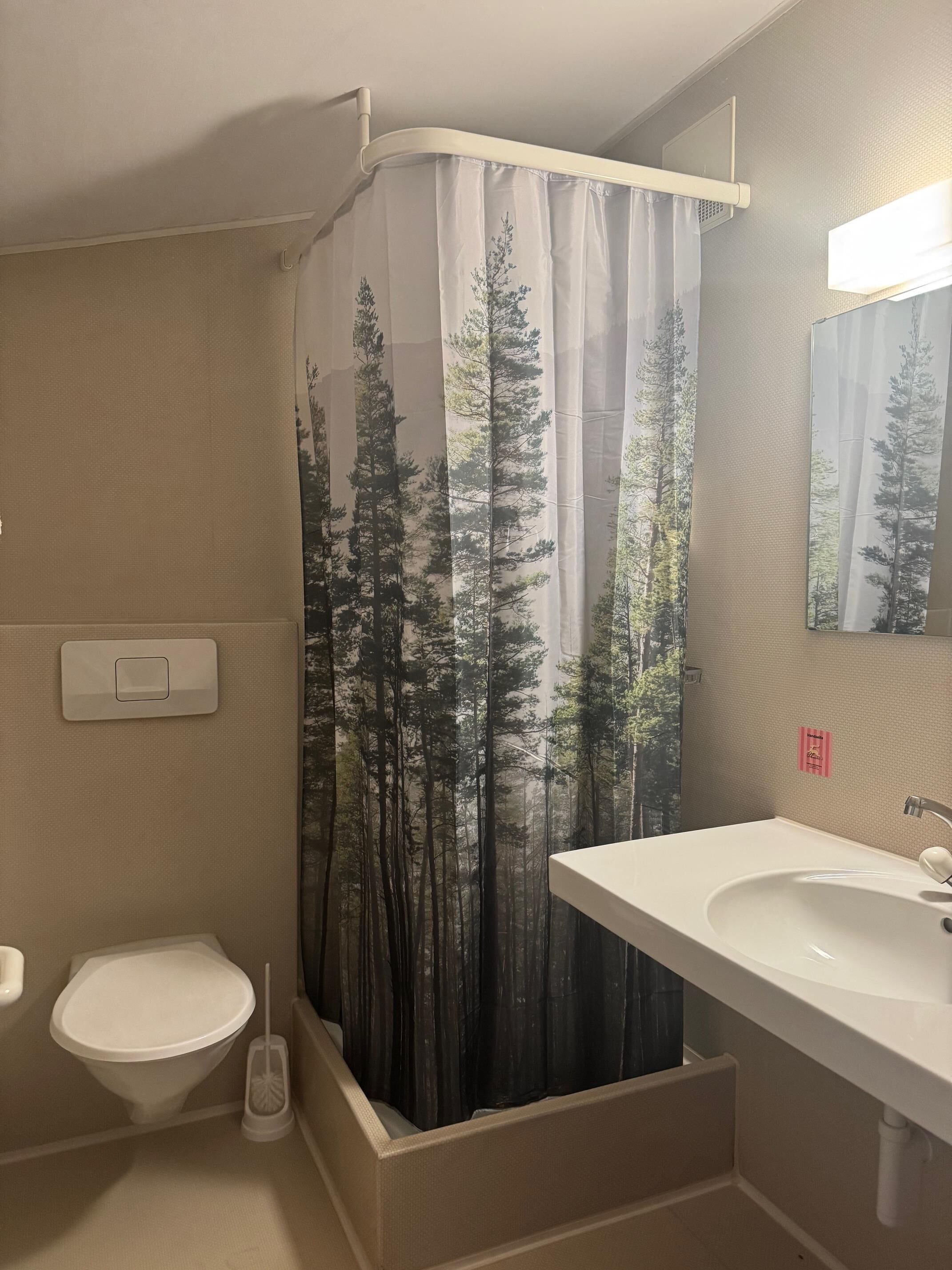 A bathroom with a toilet, sink, and shower curtain with a forest print.