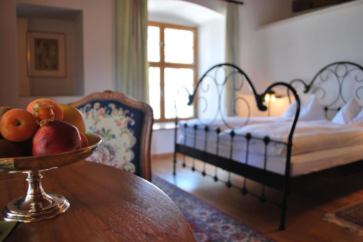 A room with a bed, a table with a fruit bowl, and a chair.