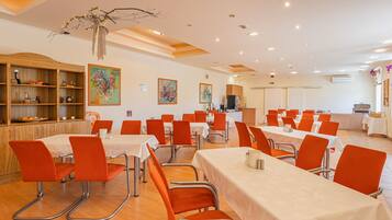 A dining area with tables and chairs, a wooden cabinet with dishes, and artwork on the walls.