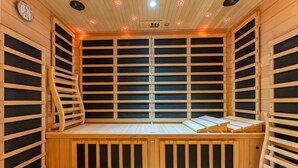 A sauna with wooden walls and benches, a ceiling with lights, and a clock on the wall. - Oázis Hotel Apartments (Nagykanizsa)