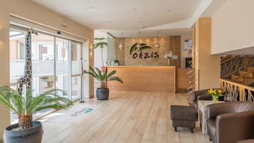 Un área de recepción con un mostrador de madera, plantas en macetas y un espacio de descanso con sillones de cuero.