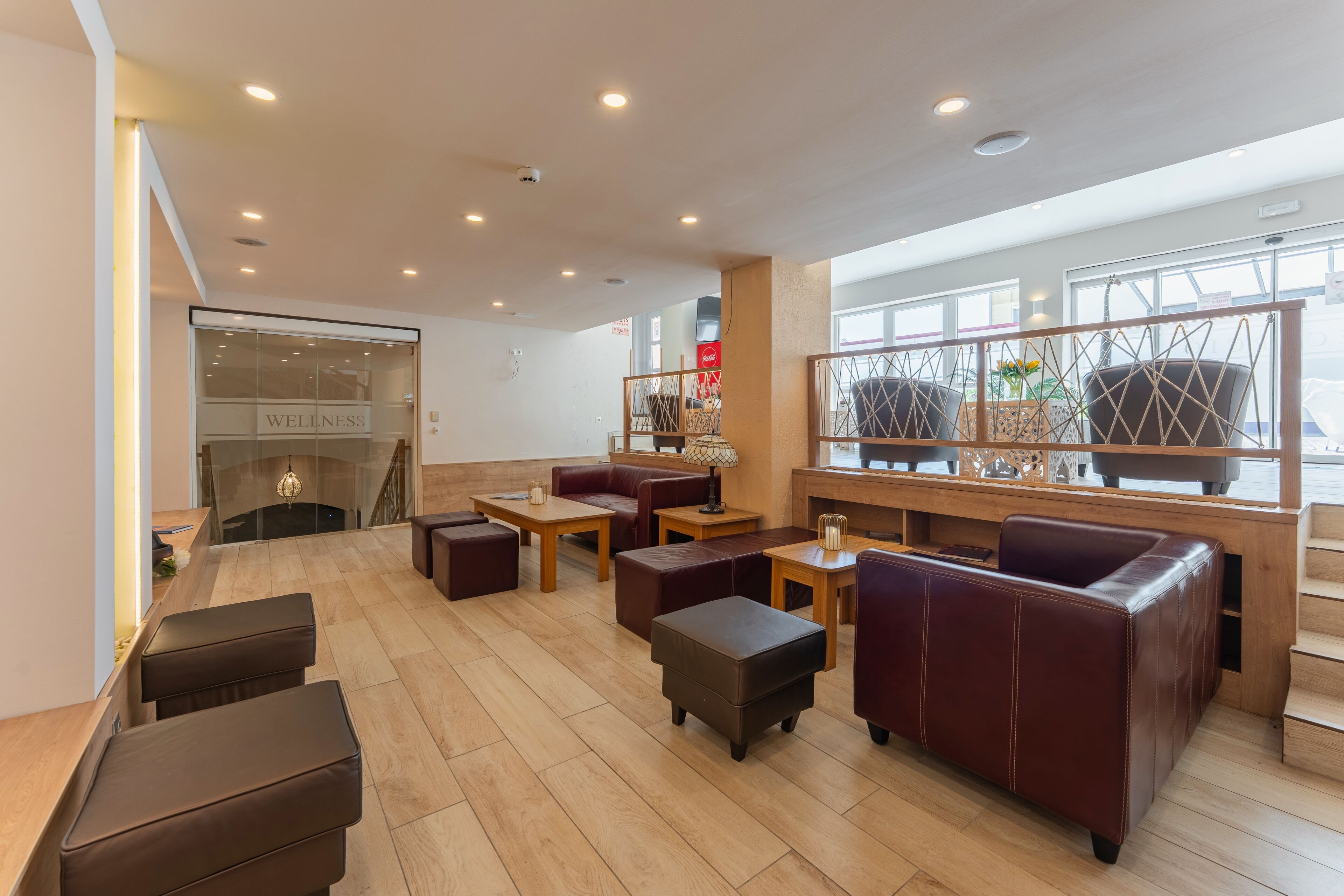 Un área de lounge moderna con sofás de cuero, mesas de madera y una pared de vidrio con un cartel que dice 'Wellness'.