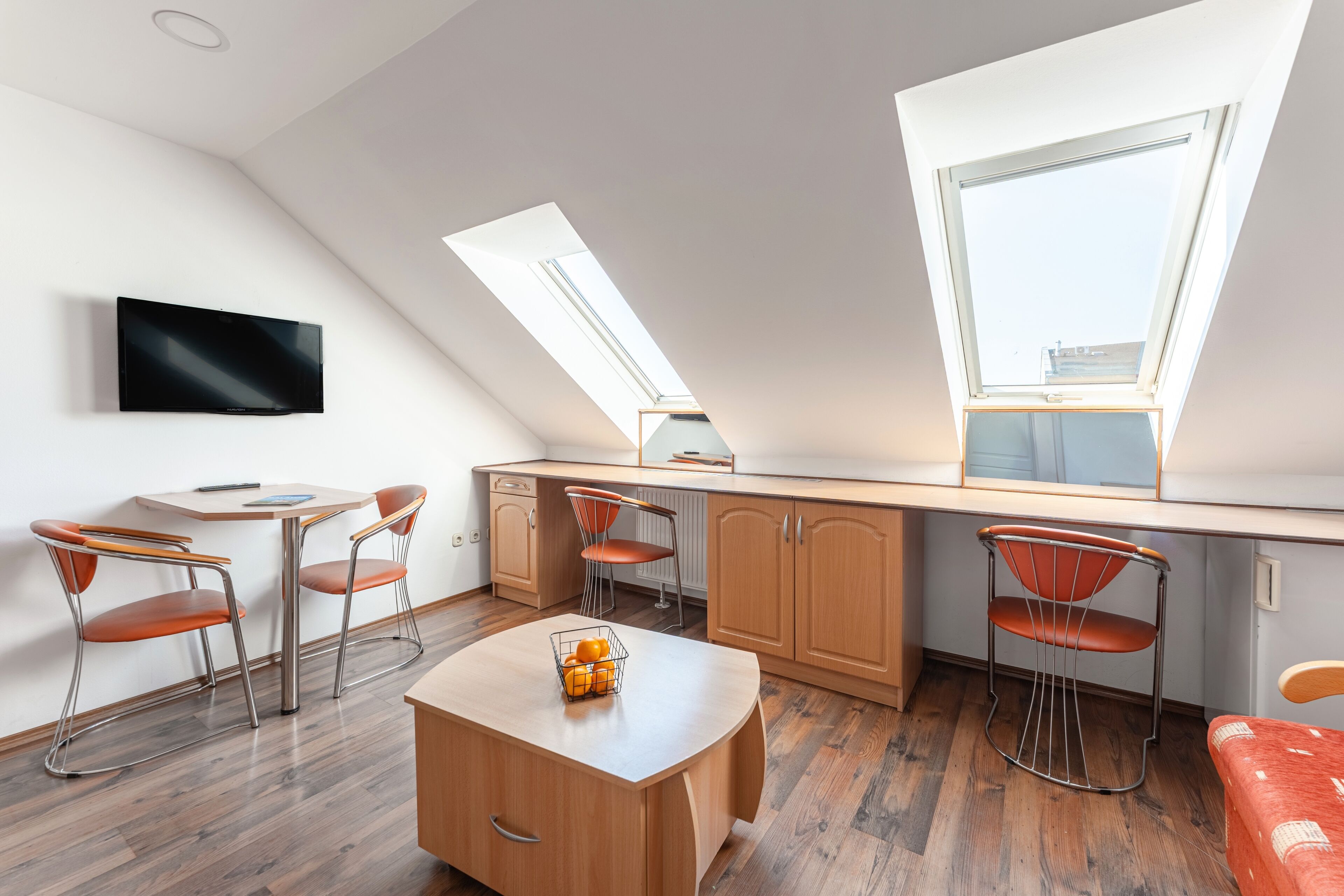 A modern kitchen with a dining area, featuring skylights, wooden cabinets, and a flat-screen TV.